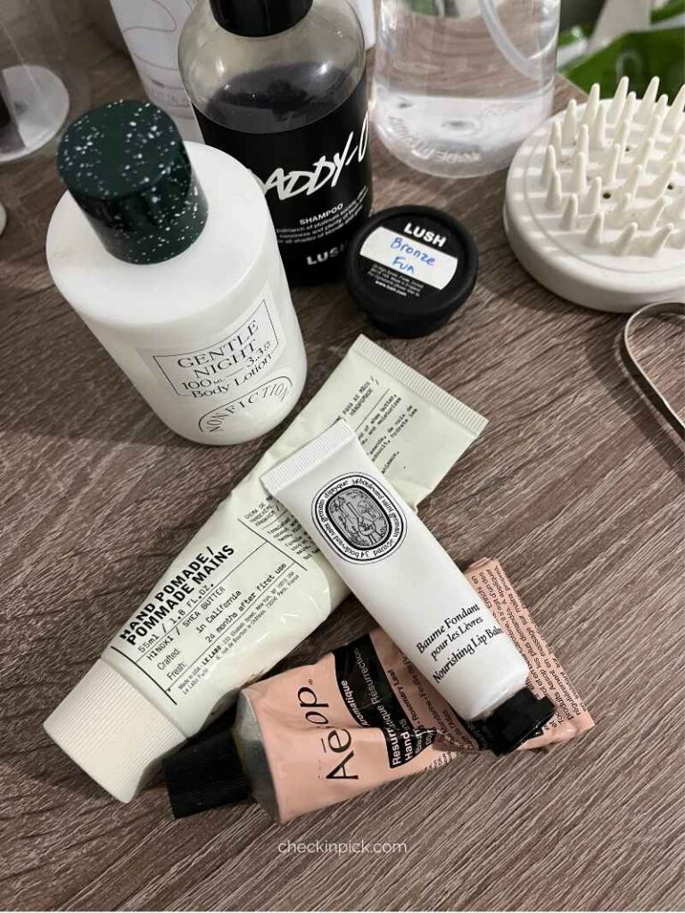 Travel toiletries including hand cream, lip balm, body lotion, scalp massage brush, and shower jelly packed for a London trip